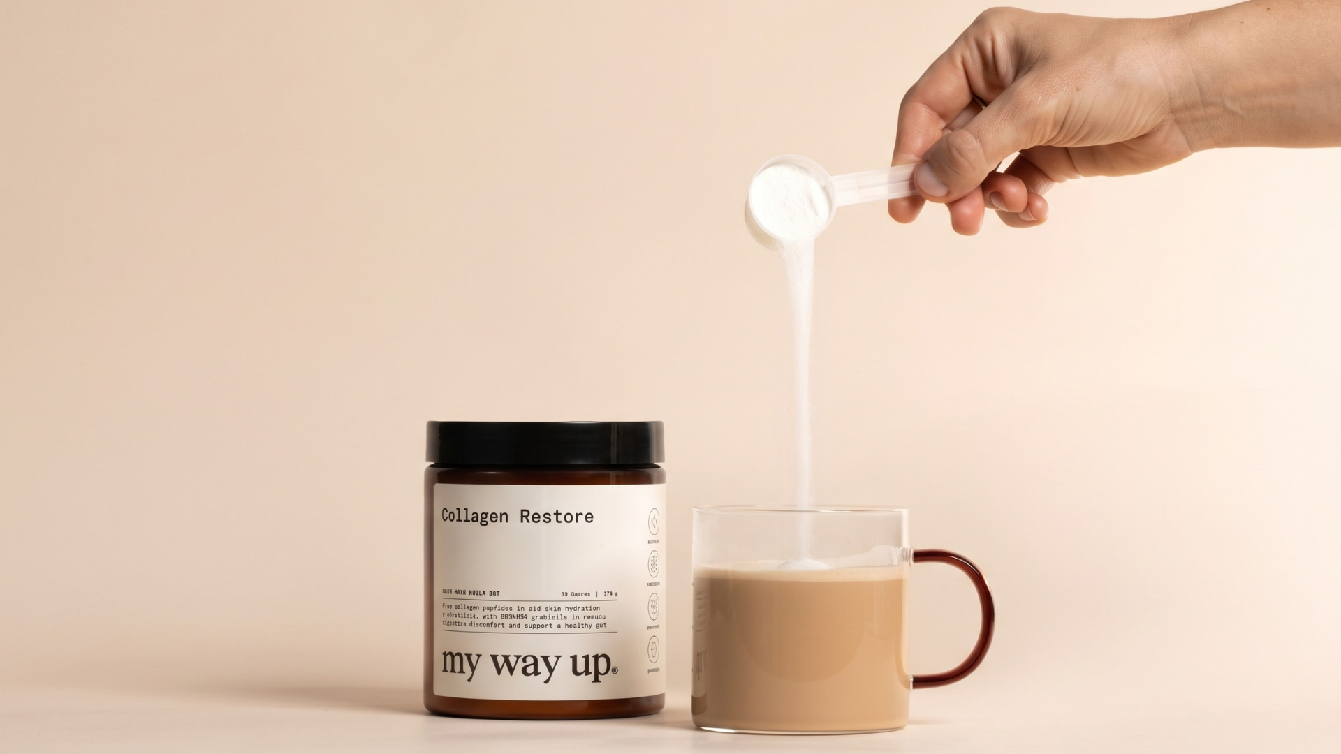 Hand pouring a scoop of Collagen Restore powder into a glass mug of milky coffee, next to a jar of My Way Up Collagen Restore